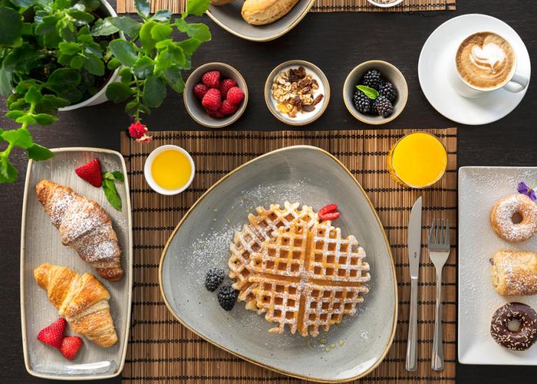 Colazione con waffle, croissant, frutta, succo e caffè.